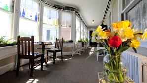 A sunlit room with a chessboard, chairs, a vase of flowers, and a radiator. - Brewster Inn (Dexter)