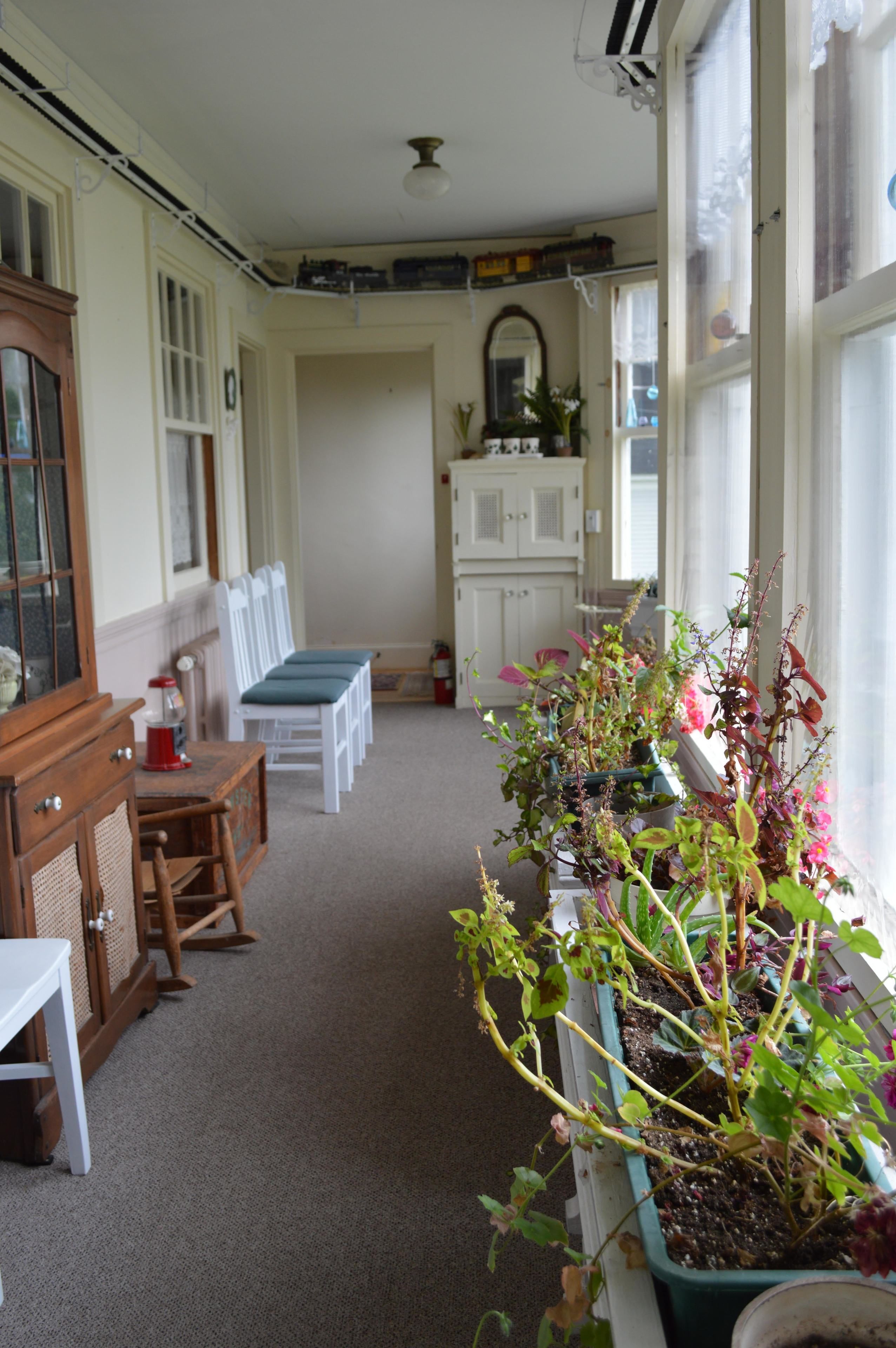 A room with a wooden cabinet, a white table with blue chairs, a potted plant, and a window with curtains.