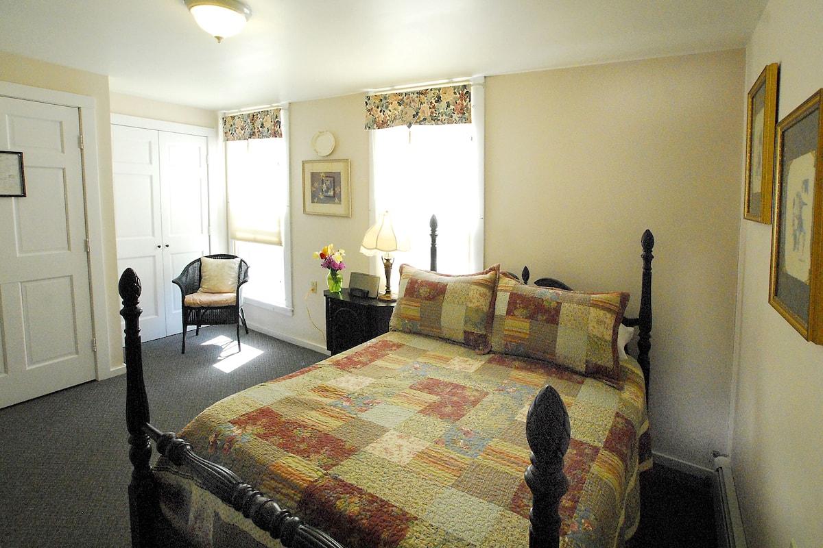 A bedroom with a large bed, a chair, a nightstand, and a window with curtains.