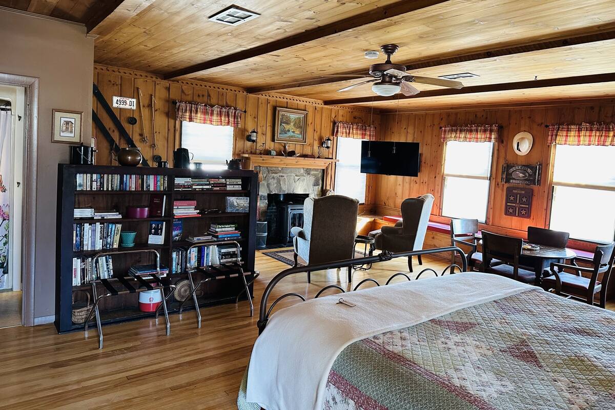 A cozy cabin-style room with a bed, a bookshelf, a fireplace, and a dining area.