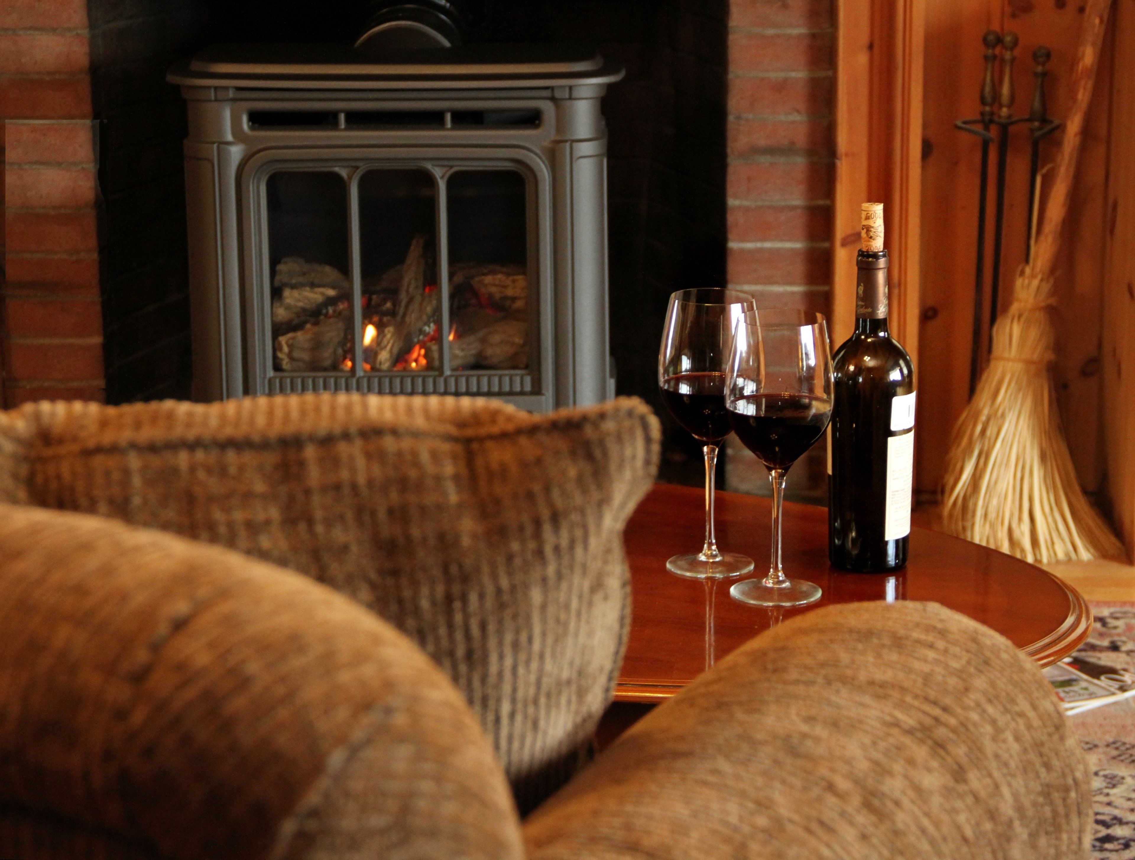 A cozy living room with a fireplace, two wine glasses, and a bottle of wine on a wooden table.