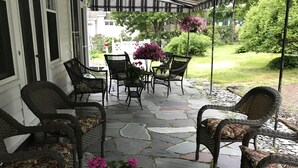 A covered patio with wicker furniture and a stone floor, featuring a table with a potted plant.
