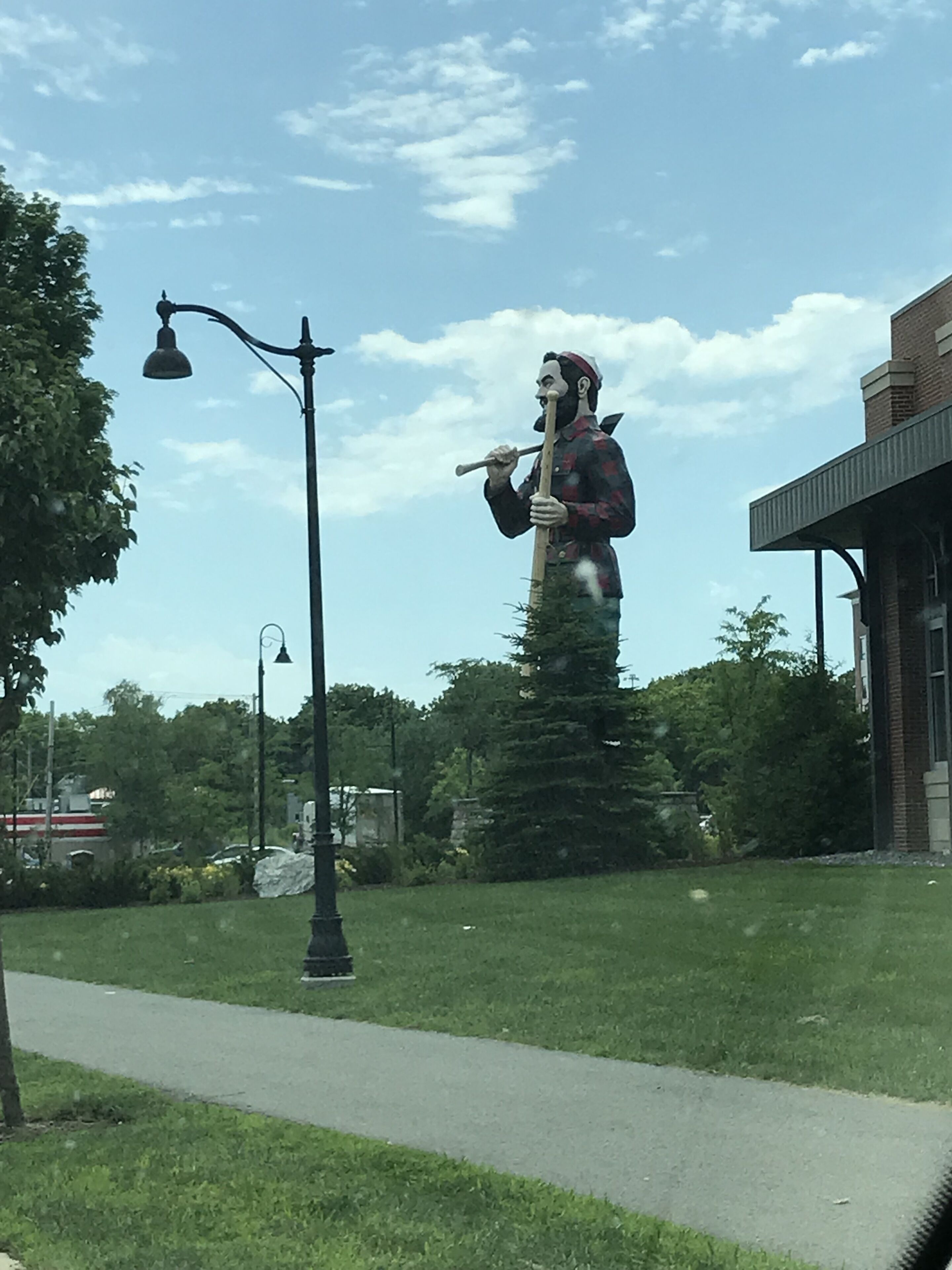 Una estatua de un hombre sosteniendo un horcón en un parque, con un edificio al fondo.