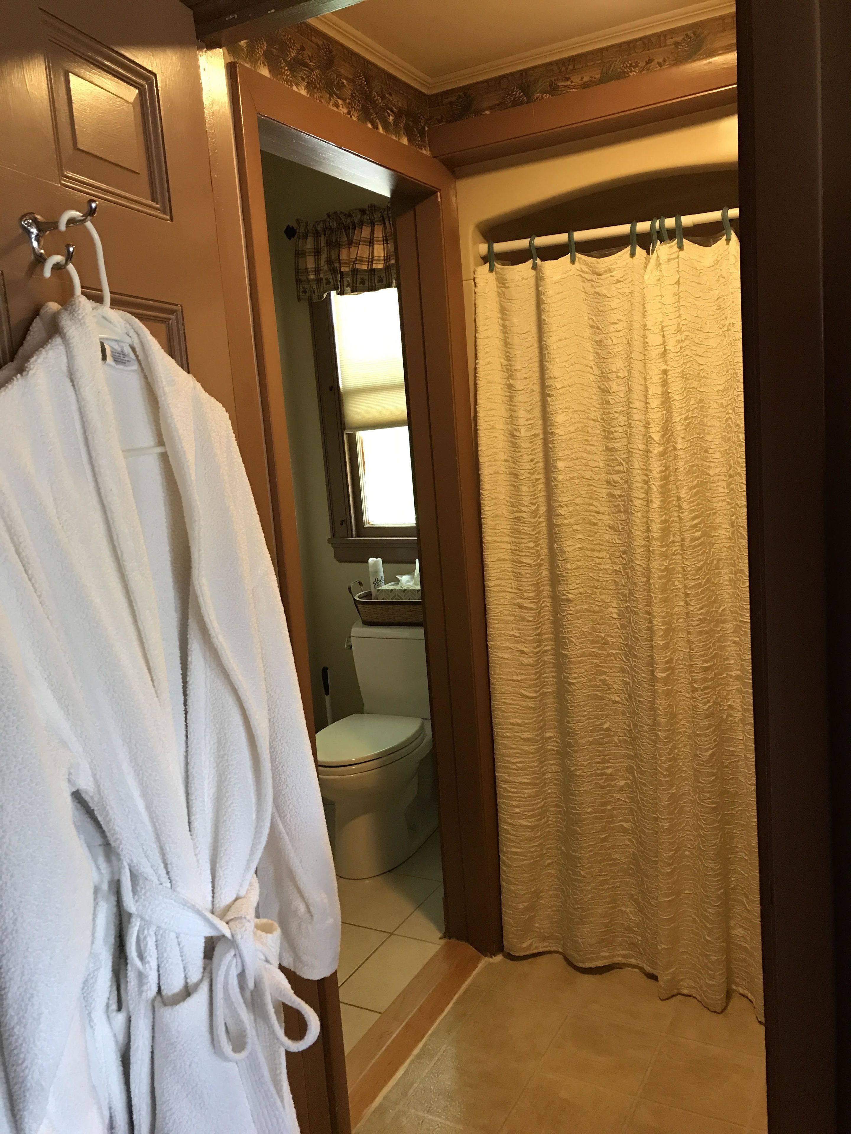 Une salle de bain avec une robe blanche suspendue à un crochet, des toilettes et un rideau de douche.