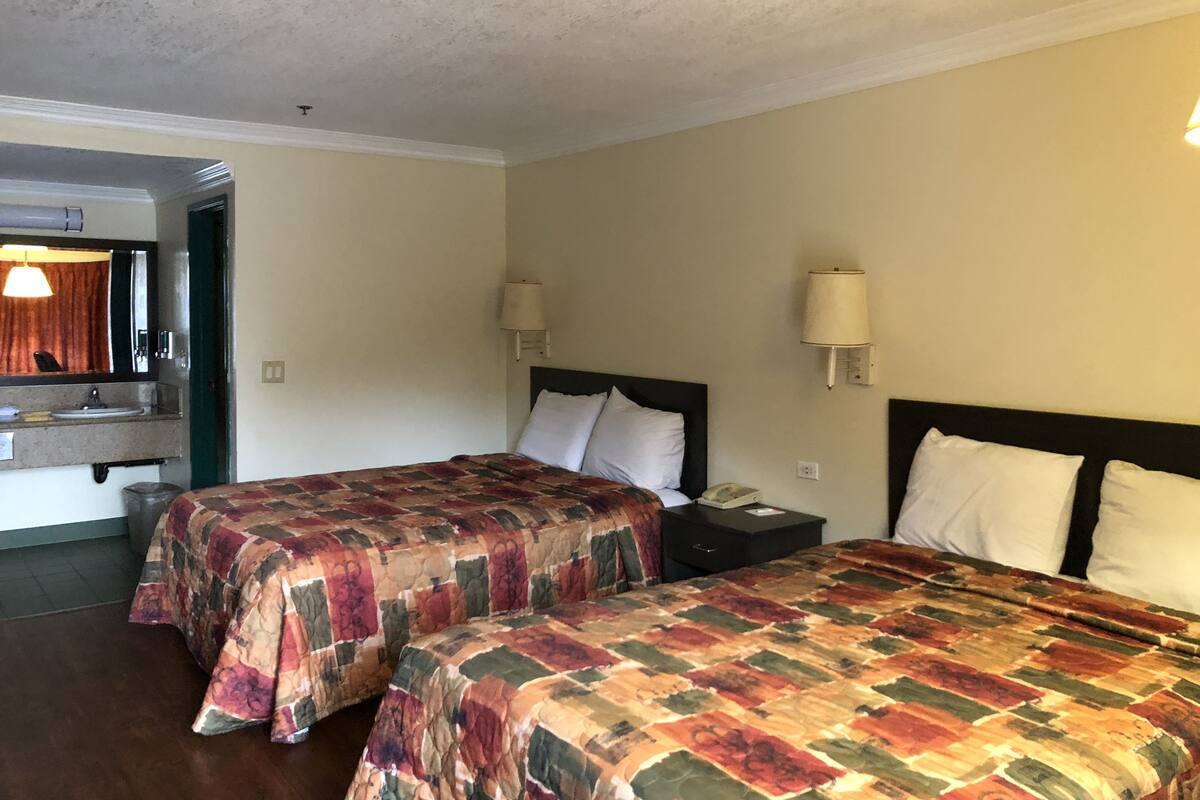 A hotel room with two beds, a bathroom, and a small desk.