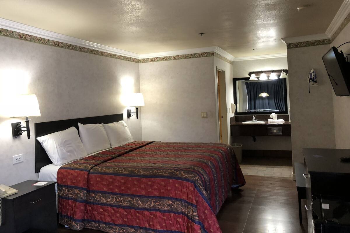 A hotel room with a bed, bedside lamps, a desk with a telephone, a mirror, and a bathroom with a sink and mirror.