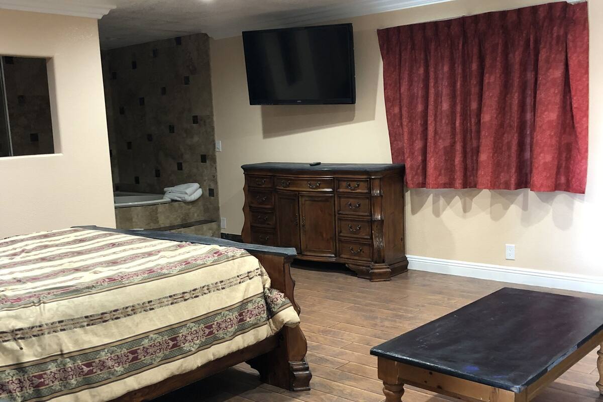 A bedroom with a bed, a wooden dresser, a television, and a red curtain.