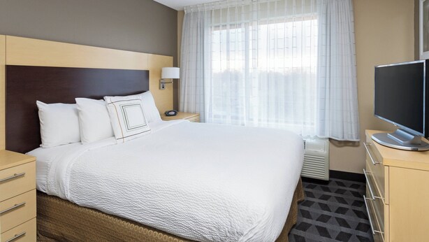 Hotellihuone, jossa on suuri sänky, taulutelevisio, yöpöytä ja ikkuna, jossa on läpikuultavat verhot.