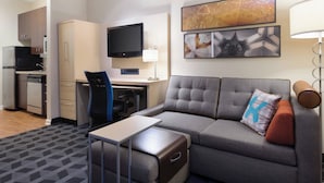 Kompakti hotellihuone, jossa on sohva, pieni työpöytä, televisio ja pieni keittiö.