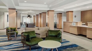 Un vestíbulo moderno con mostrador de recepción, zona de estar con sillones tapizados en verde, una mesa redonda y una escalera que lleva a un nivel superior.