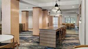 Un lobby moderno de hotel con bar central, zona de estar y amplias ventanas.