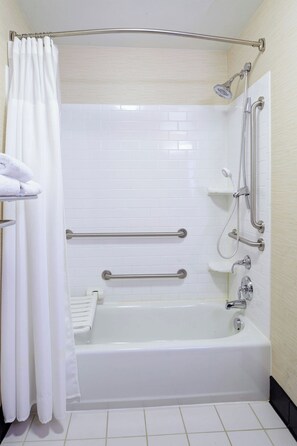 Un baño con una bañera blanca, barras de apoyo, cabezal de ducha y un perchero para toallas.