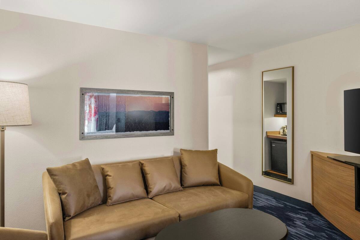 A hotel room with a sofa, a small table, a mirror, and a television.