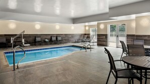 Zona de piscina con suelo de baldosas, sillones de descanso y una mesa.