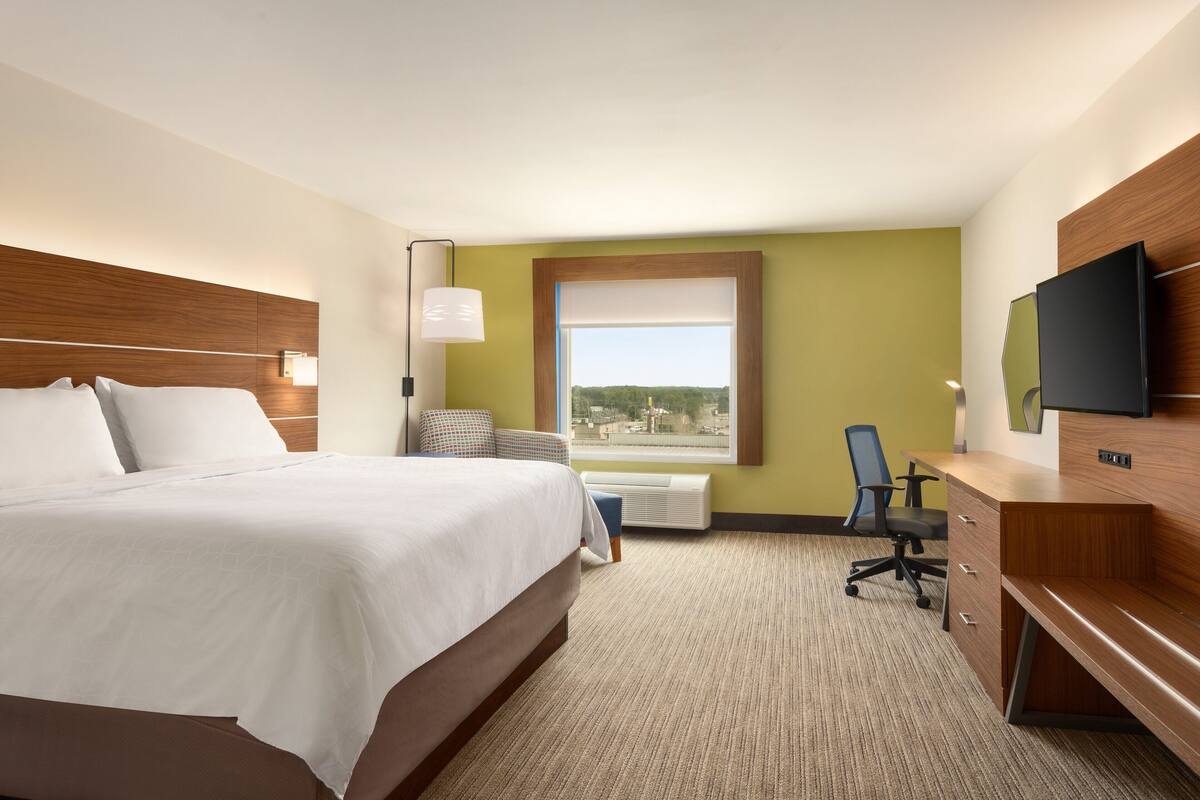 Une chambre d’hôtel avec un grand lit, un bureau, une chaise, une télévision et une fenêtre donnant sur un beau paysage.