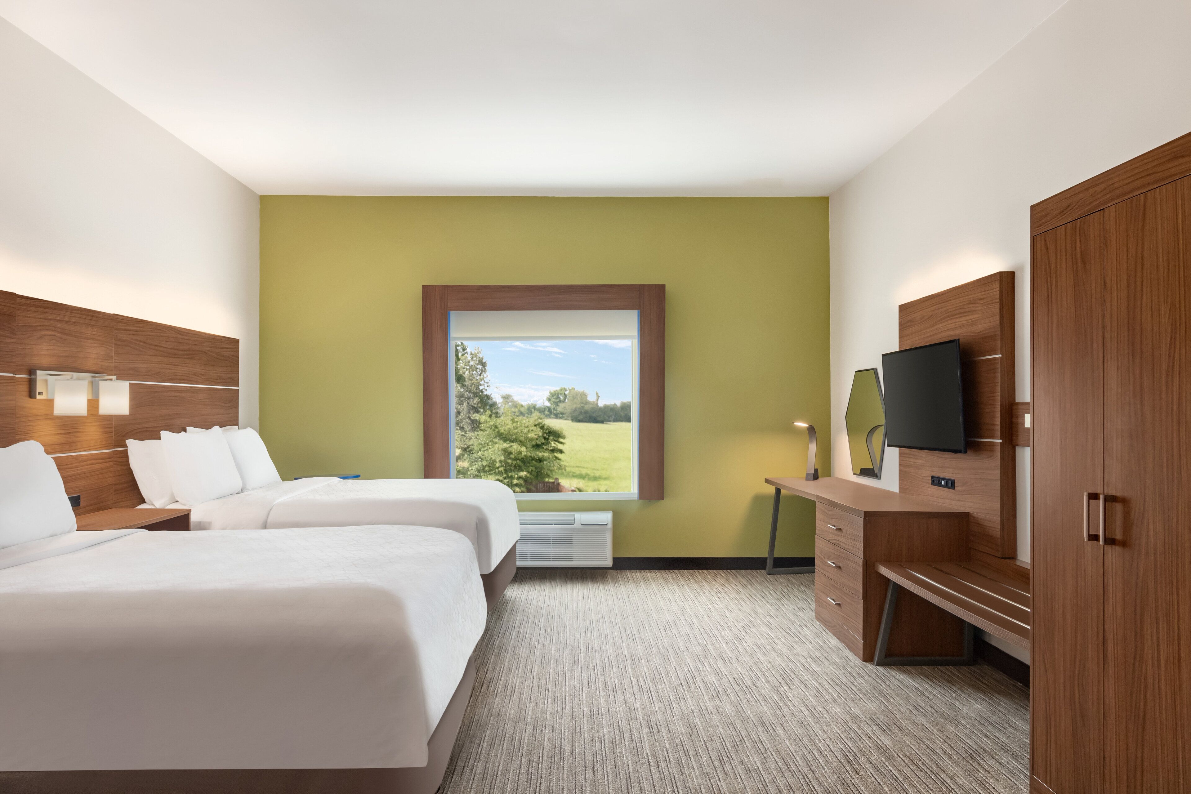 Habitación de hotel con dos camas, un ventanal con vistas a la vegetación, un televisor de pantalla plana y un armario de madera.
