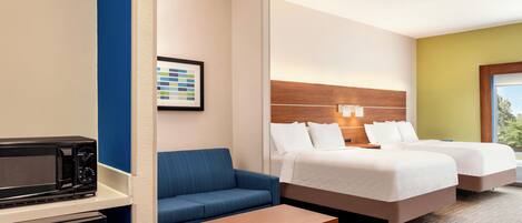 A hotel room with a kitchenette, a sofa, two beds, and a small table.