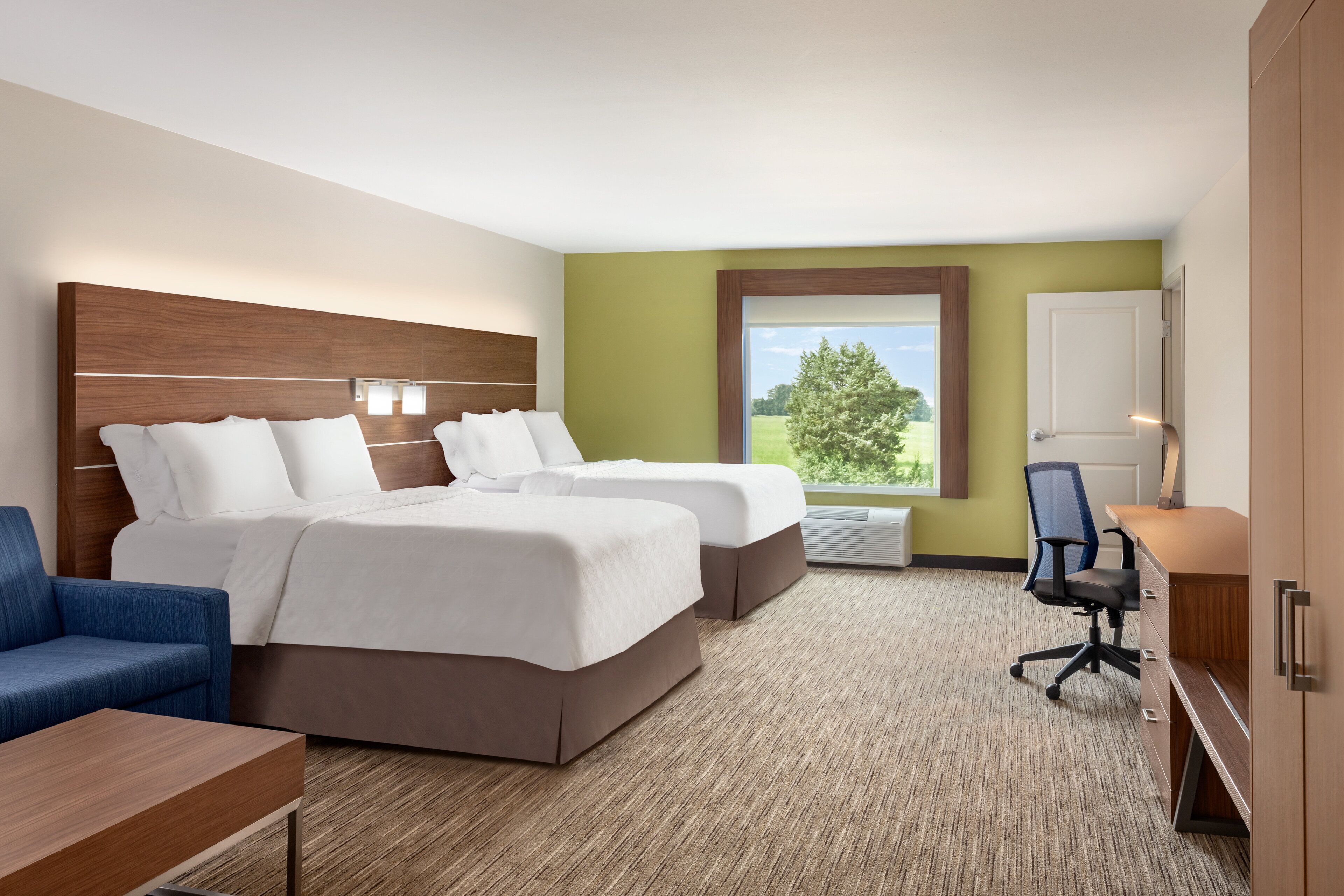 Quarto de hotel com duas camas, uma escrivaninha, uma cadeira e vista para o exterior.