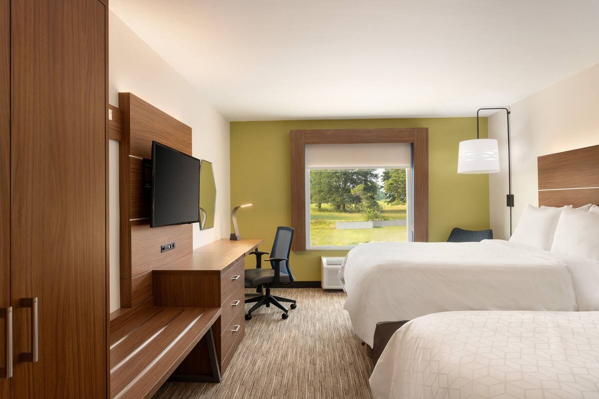 Une chambre d’hôtel comprenant un lit, un bureau avec une chaise, une télévision et une fenêtre donnant sur des arbres.
