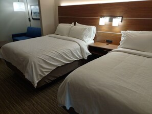 A hotel room with two beds, a wooden headboard, a nightstand, and a blue chair.