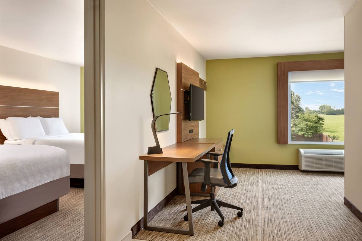 Une chambre d’hôtel comprenant un lit, un bureau avec une chaise, un téléviseur à écran plat et une fenêtre donnant sur un paysage verdoyant.