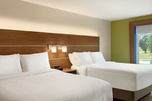 A hotel room with two beds, a wooden headboard, bedside lamps, and a window with a view of greenery.