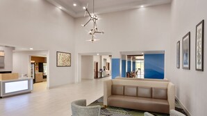 A spacious lobby with a modern sofa, two armchairs, a round table, and a unique chandelier.