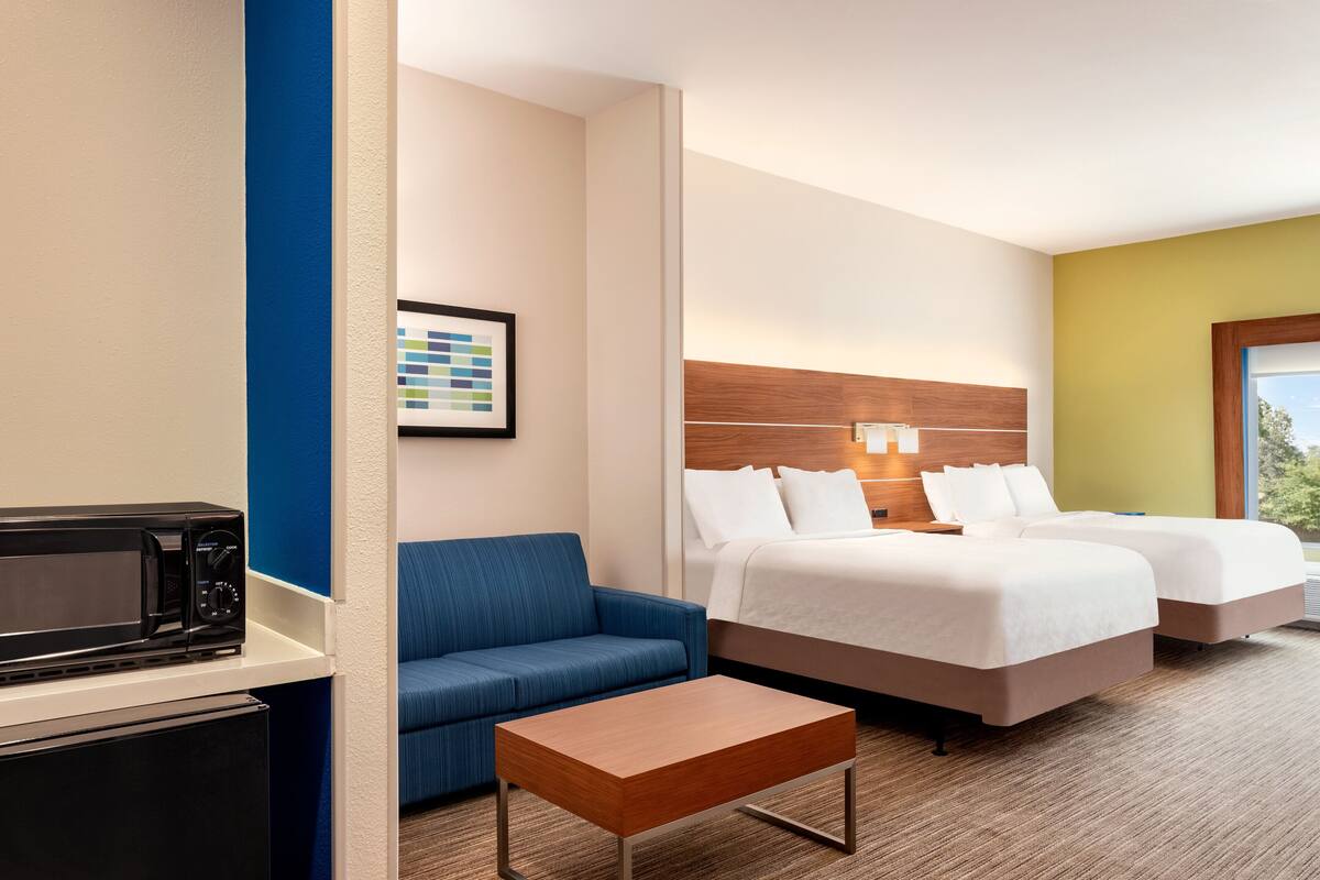 Une chambre d’hôtel comprenant un lit, deux tables de chevet, un canapé, un four à micro-ondes et un petit réfrigérateur.