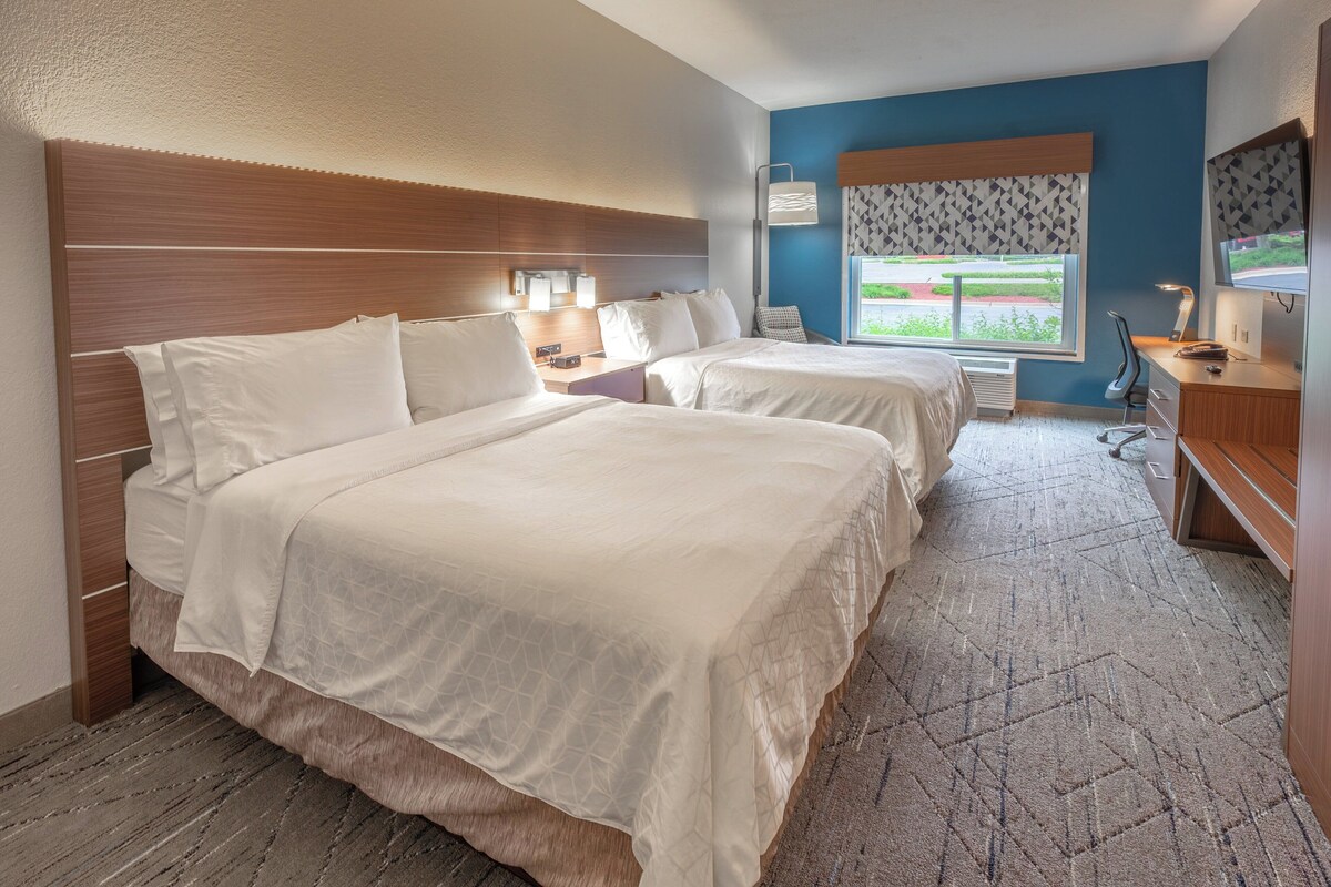 A hotel room with two beds, a desk, a chair, a TV, and a window with a view.