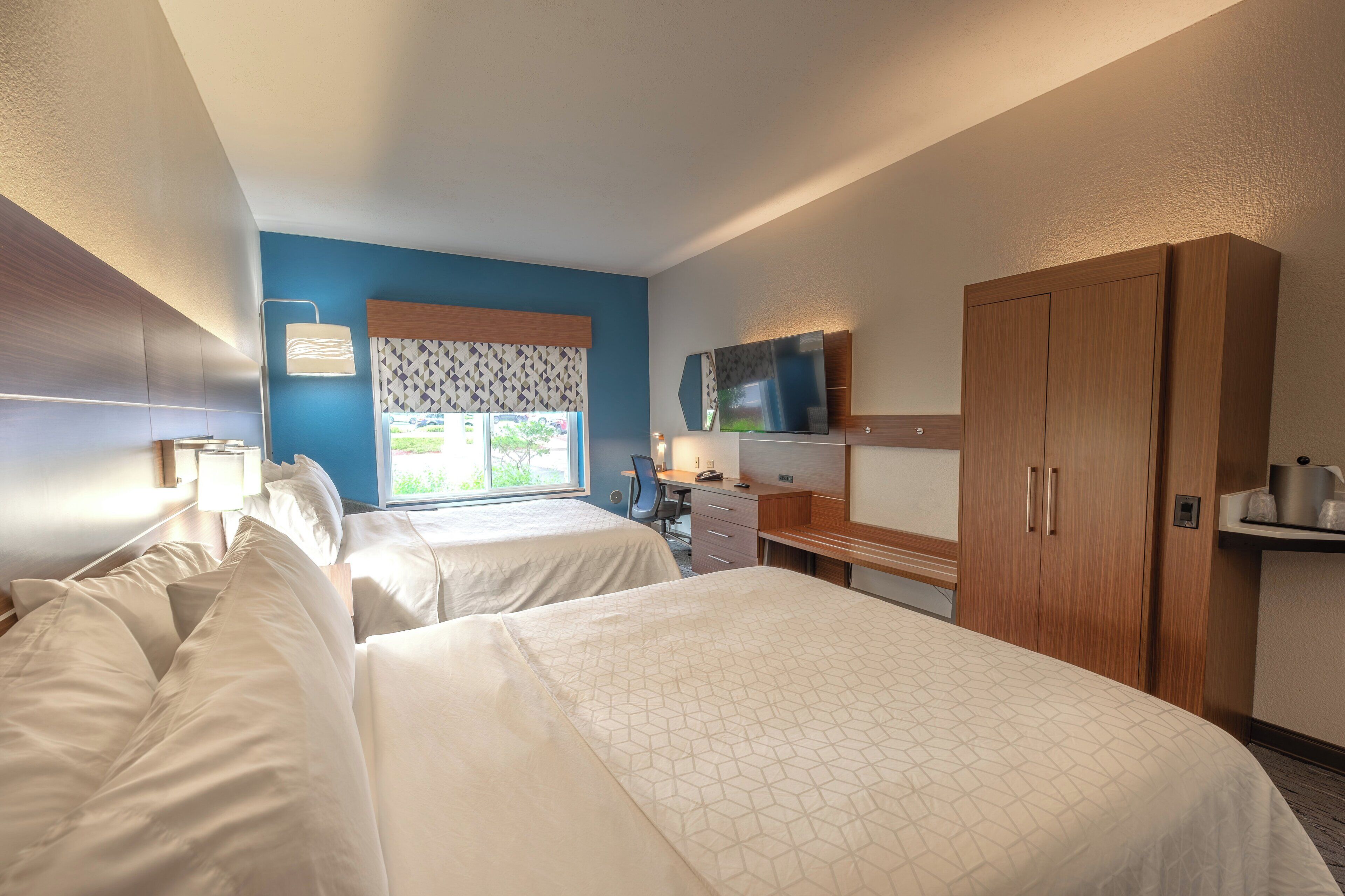 Habitación de hotel con dos camas, un escritorio, un armario y ventana con vistas.