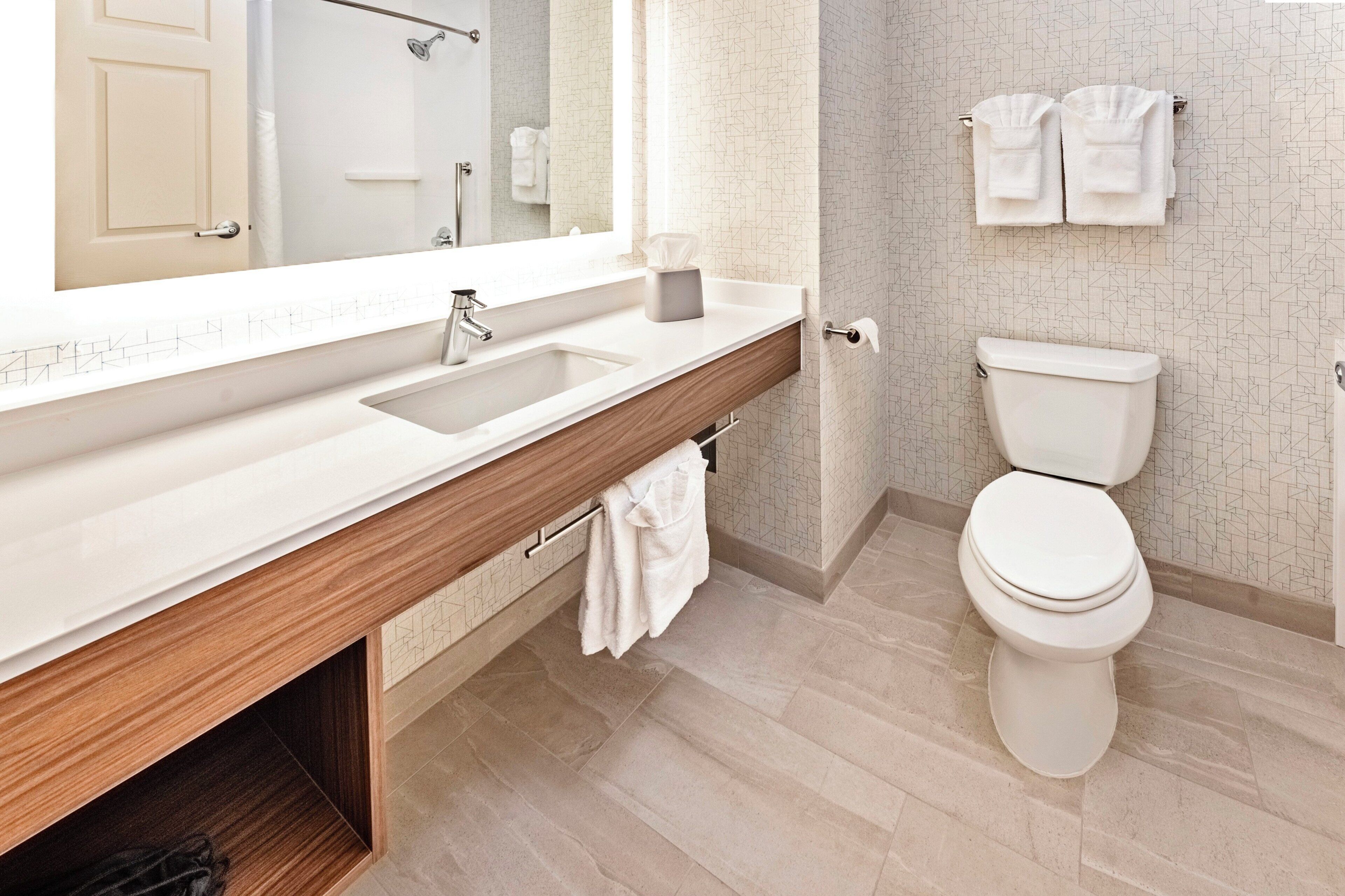 A modern bathroom with a large mirror, a sink, a toilet, and a towel rack.