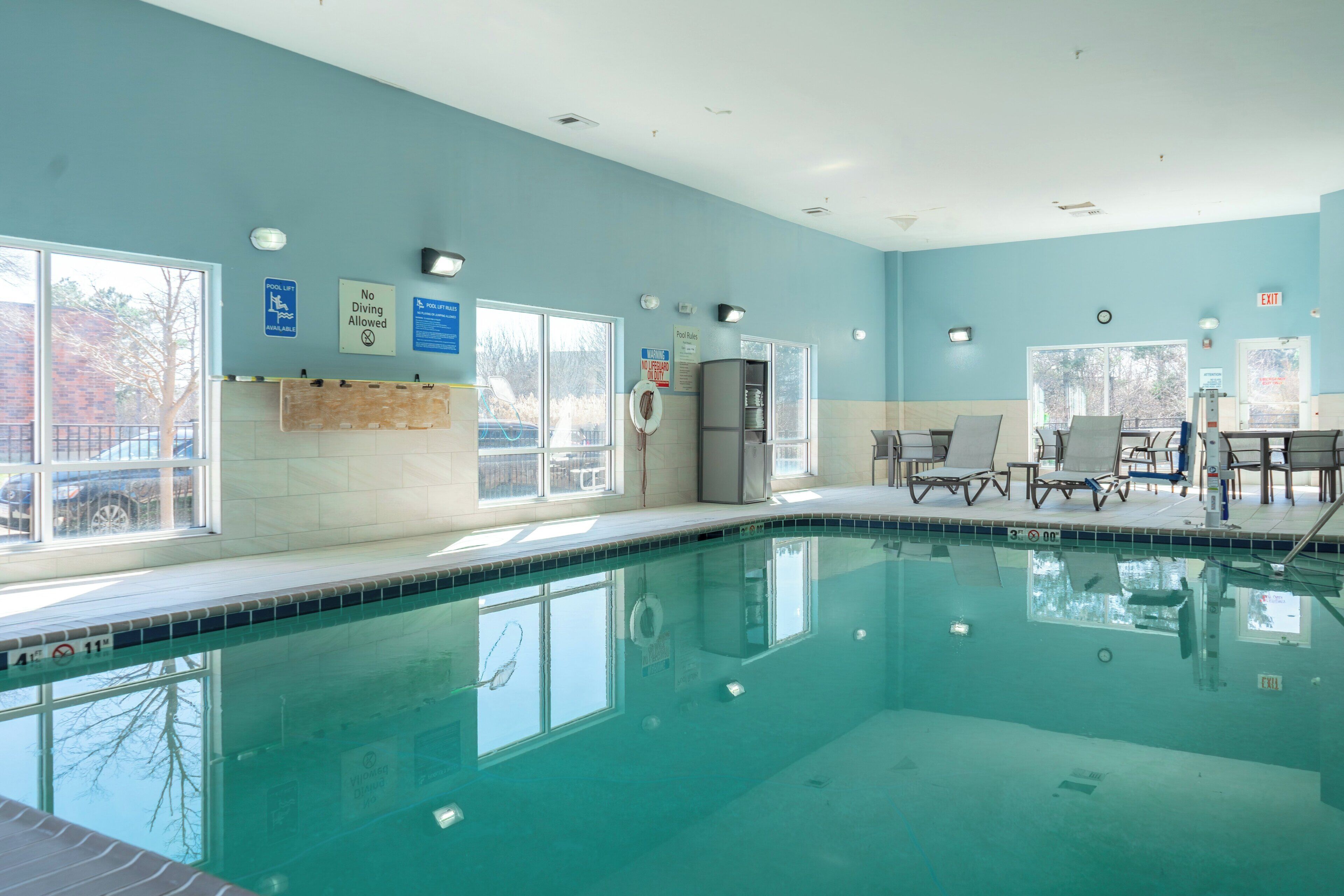An indoor swimming pool with clear windows, a lifeguard chair, and a seating area with tables and chairs.