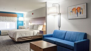 A hotel room with a bed, a blue sofa, a bedside table, a lamp, and a painting on the wall. - Holiday Inn Express Hotel & Suites, a Lake Zurich-Barrington by IHG (Lake Zurich)