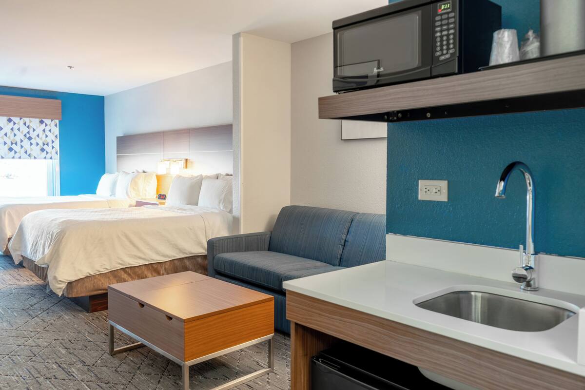 A hotel room with a bed, a sofa, a small table, a microwave, and a sink.
