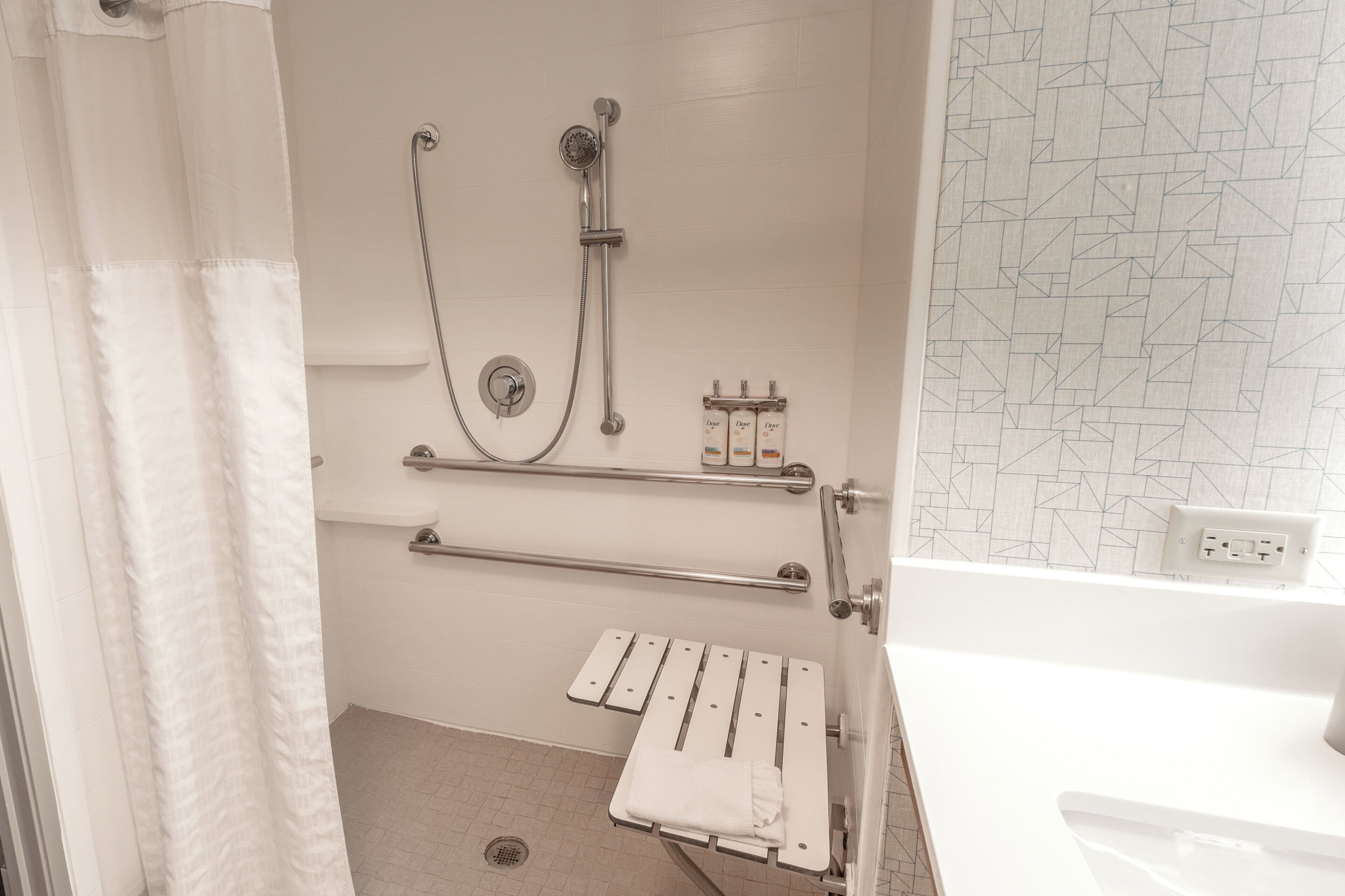 A bathroom with a shower, grab bars, a towel rack, and a tiled floor.