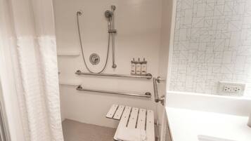 A bathroom with a shower, grab bars, a towel rack, and a tiled floor.