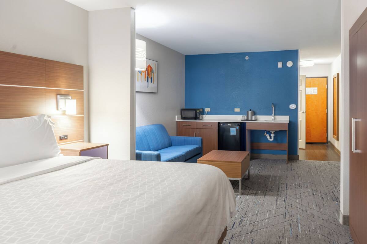 A hotel room with a bed, a blue sofa, a kitchenette, and a bathroom.