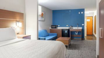 Quarto de hotel com uma cama, um sofá azul, uma cozinha compacta e um banheiro.