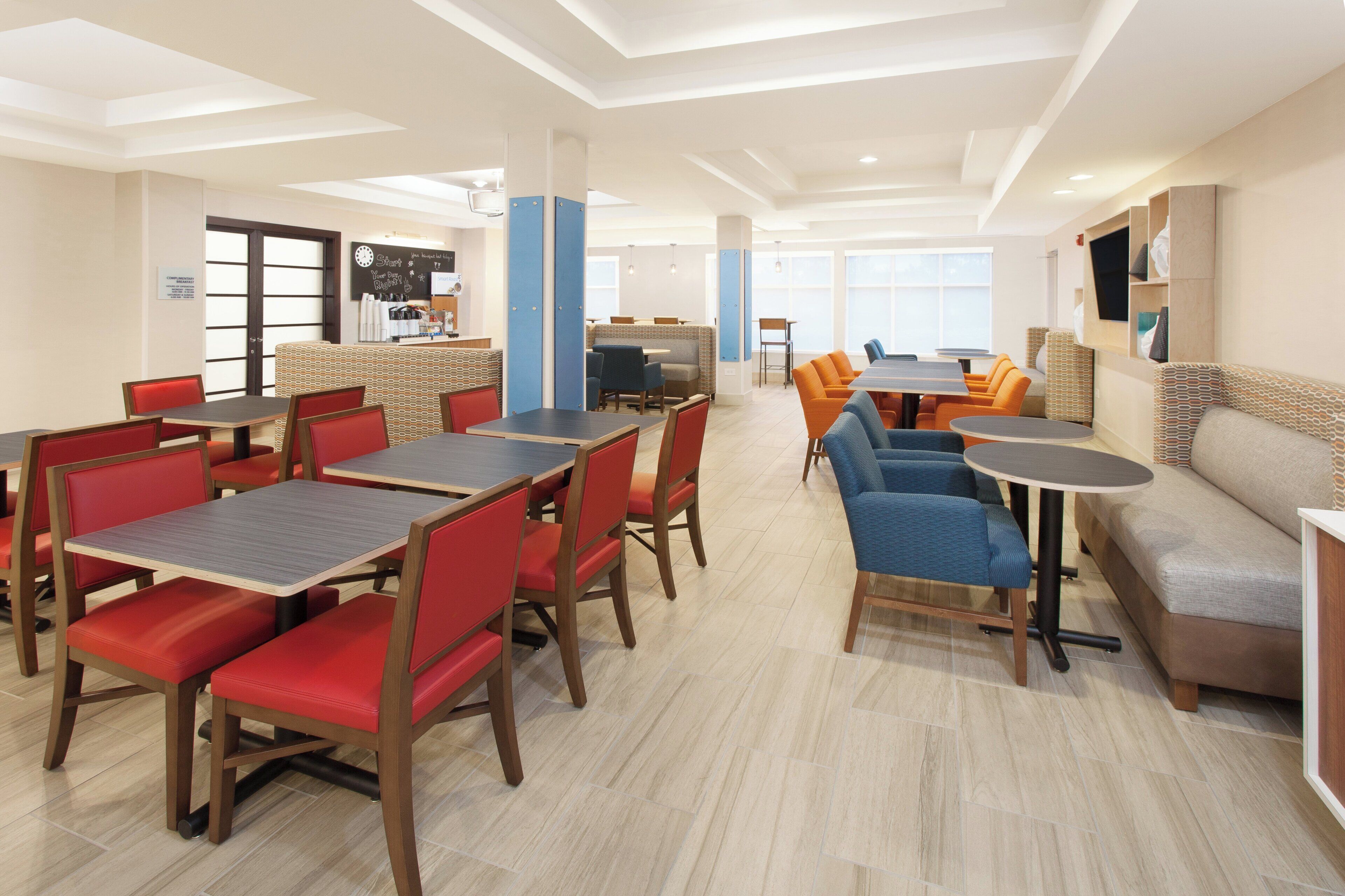 Un comedor moderno con varias mesas y sillas, una estación de café y una zona de estar con sofá.