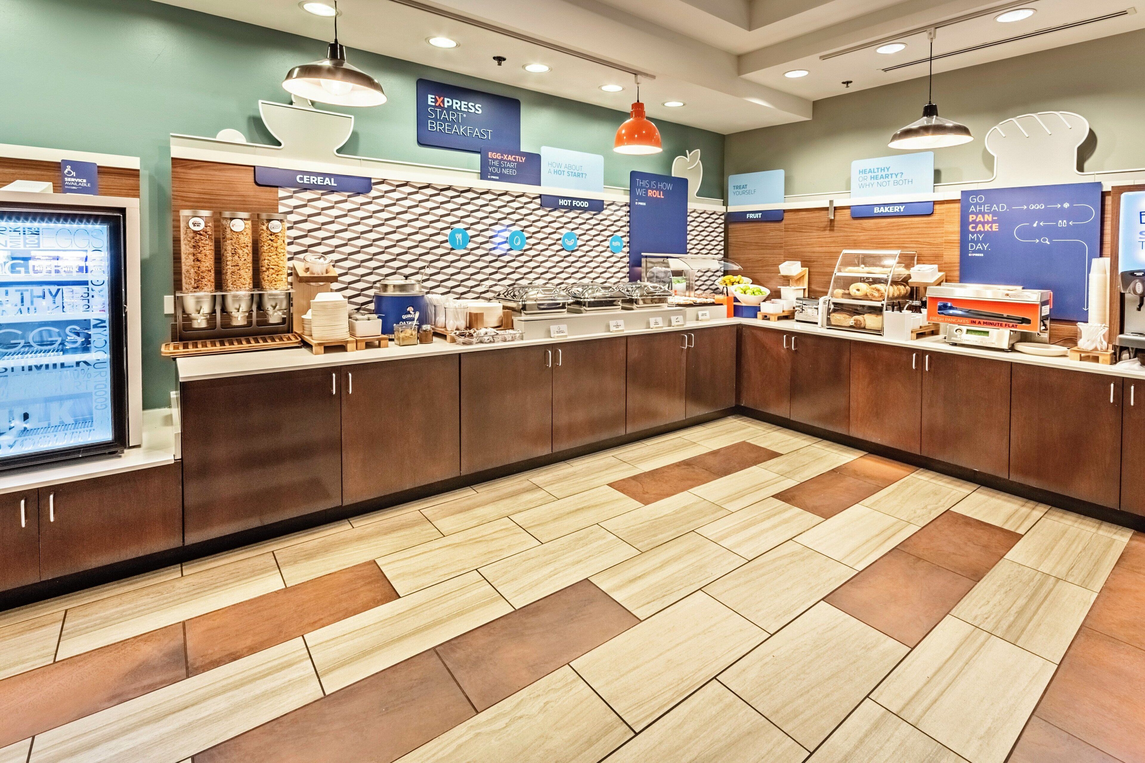 Un espace buffet pour le petit-déjeuner avec différents stands proposant une variété d’aliments, notamment des céréales, des plats chauds et des produits de boulangerie.
