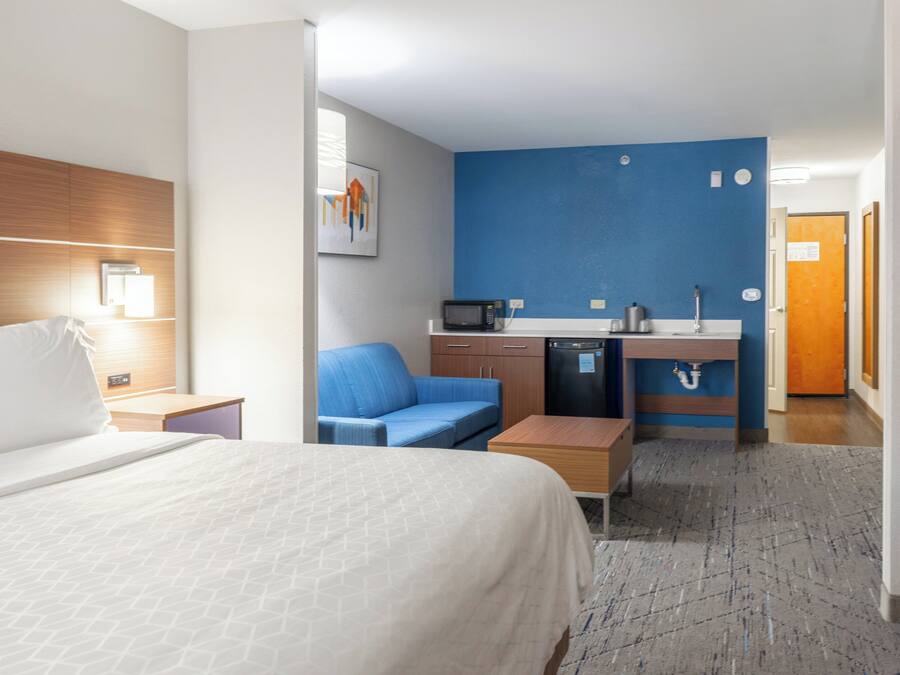 Quarto de hotel com uma cama, um sofá azul, uma cozinha compacta e uma pequena mesa.
