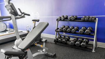 A gym with a bench, dumbbells, and a treadmill.