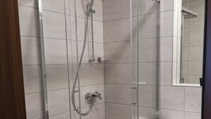 Cabina de ducha con paredes de vidrio, cabezal de ducha de mano y grifo empotrado.
