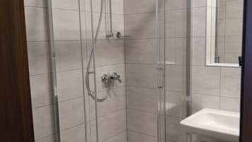 Eine Duschkabine aus Glas mit Handbrause und am Wand montierter Armatur.