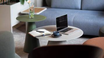 Un espace de vie moderne avec un ordinateur portable posé sur une table ronde, un carnet, un stylo et une tasse sur une soucoupe.