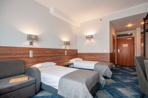 A hotel room with two single beds, a sofa, a desk, and a chair.