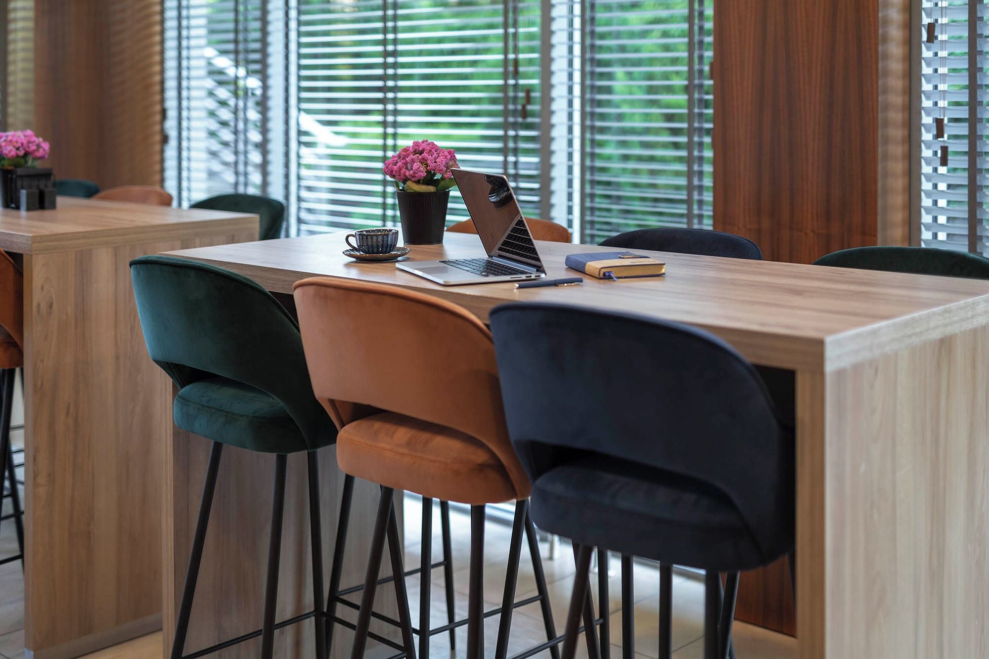 A modern conference room with a wooden table, black and teal chairs, a laptop, a cup, and a vase with flowers.