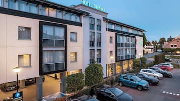 Un hotel con fachada moderna, varios espacios de estacionamiento y cielo despejado.