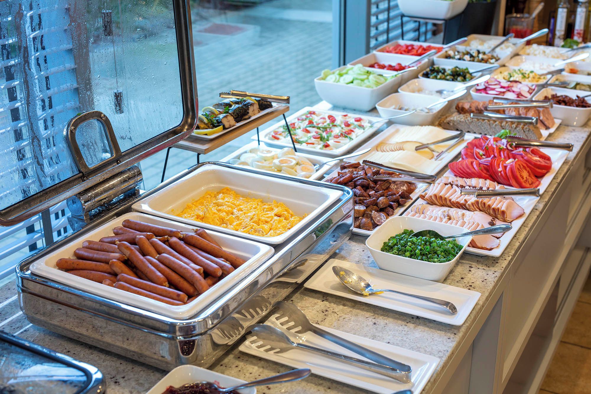 A buffet with various food options including sausages, scrambled eggs, and sliced meats.