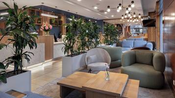 Un lobby moderno con zonas de estar, plantas y un mostrador de recepción.